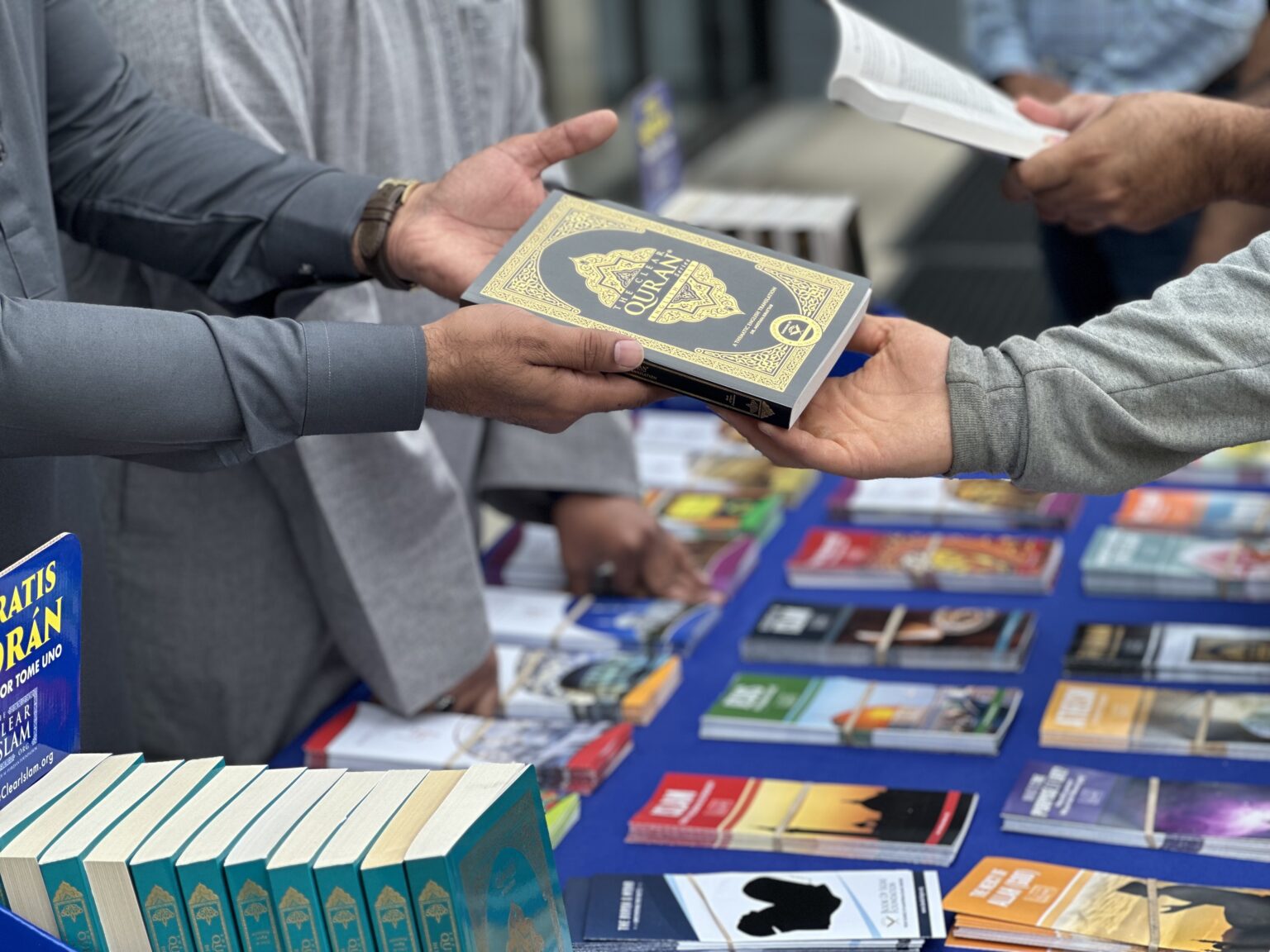 Handing a copy of The Clear Quran across a literature table